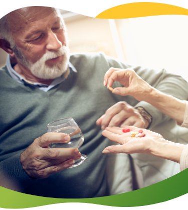 A woman hands over medicine to a man of retirement age who is is holding a glass of water
