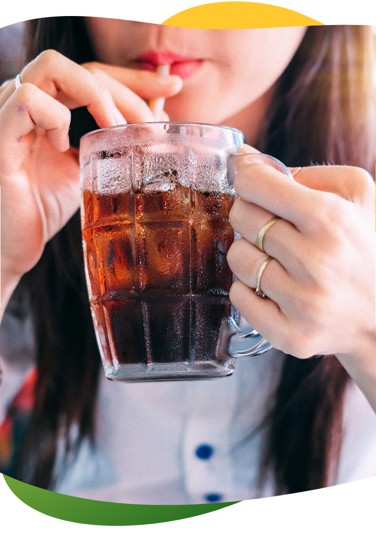 Wheat field in the bright suA young woman with long, brown hair holds a tall glass with her hand and drinks a carbonated drink with a straw out of it n