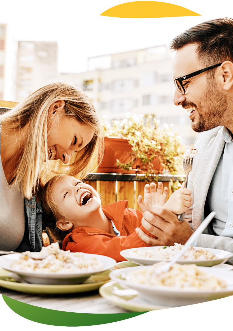Young parents having a meal at the dining table, wearing their work clothes with their child sitting between them. They are laughing and having a good time together